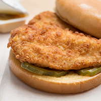 Closeup of our seasoned chicken breast on two pickles and a bun